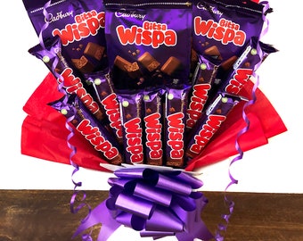 May include: A bouquet of Cadbury Wispa chocolate bars wrapped in red tissue paper with a purple ribbon. The bouquet is arranged in a white box.