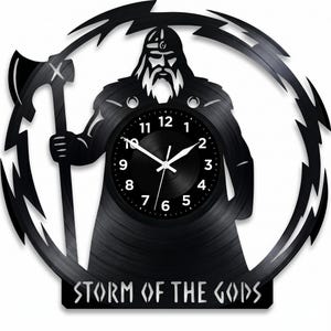 May include: Black vinyl record clock depicting a Viking warrior holding an axe, encircled by a lightning bolt design. The clock face has white numerals and hands. The text "STORM OF THE GODS" is at the bottom.