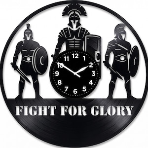 May include: Black wall clock featuring three Roman soldiers with shields and swords. The clock face is in the center, and the words "FIGHT FOR GLORY" are at the bottom. The clock is round.