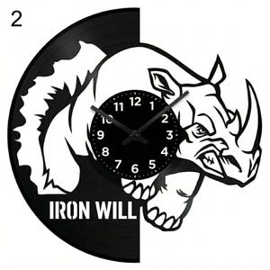 以下が含まれることがあります： 白サイのデザインが施された黒いビニールレコード時計。時計の文字盤は黒で、白い数字と針が付いています。「IRON WILL」の文字がレコードの下部にあります。