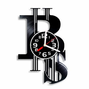 May include: Black vinyl record clock with a Bitcoin symbol design. The clock face is black with white numbers and hands. The clock is mounted on a wall.