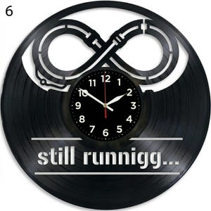 May include: A black vinyl record clock with a circular black clock face. The clock hands are white and red. The clock has a cut-out design of an infinity symbol. The text "still runnigg..." is displayed at the bottom.
