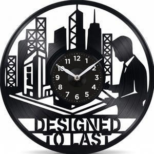 May include: Black vinyl record clock with a cityscape silhouette and a clock face. The clock features a person's silhouette and the text "DESIGNED TO LAST". The clock hands are white.