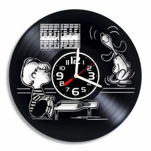 May include: Black vinyl record clock featuring Peanuts characters Charlie Brown and Snoopy. Charlie Brown is playing piano with musical notes above him; Snoopy is singing.  The clock face is centrally located with black and white numbers.  The overall design is minimalist and stylish, suitable for music lovers and Peanuts fans.