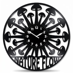 Puede incluir: Reloj de pared negro con un diseño único con forma de hongo que irradia desde una esfera central. La esfera es negra con números y manecillas blancas. Las palabras "NATURE FLOW" están recortadas en la parte inferior.