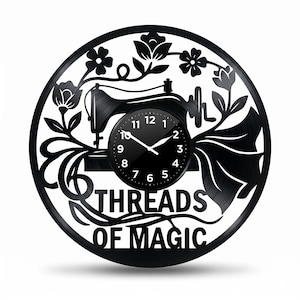 Op de afbeelding: Zwarte vinylplaat klok met een silhouet van een naaimachine, bloemmotieven en de tekst "THREADS OF MAGIC". De klok heeft een zwarte wijzerplaat met witte cijfers en wijzers. Een decoratief item voor een naaikamer.
