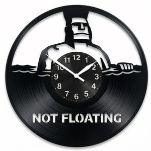 May include: Black vinyl record clock featuring a silhouette of a Moai statue in water. The clock face is black with white numbers and hands. The words "NOT FLOATING" are cut out at the bottom.