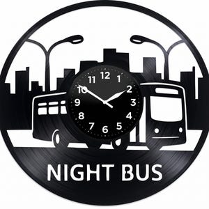 Può includere: Orologio in vinile nero con una silhouette dello skyline della città con due autobus e lampioni. Il quadrante dell'orologio è nero con lancette e numeri bianchi. Le parole "NIGHT BUS" sono in basso.