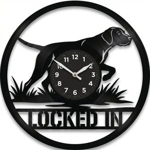 May include: Black wall clock featuring a silhouette of a dog in motion, with a clock face at the center. The clock has a black border and the words "LOCKED IN" at the bottom. The clock hands show the time.