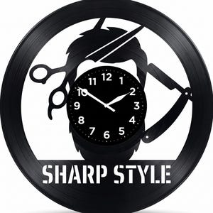 Puede incluir: Reloj de vinilo negro con temática de barbería. El reloj presenta una silueta de barba, tijeras y una navaja. La esfera del reloj es negra con números y manecillas blancas. El texto "SHARP STYLE" está en la parte inferior.