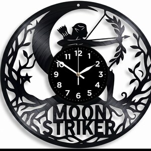 May include: Black vinyl record clock featuring a silhouette of an archer aiming a bow and arrow, set against a crescent moon and tree branches. The clock face is black with white numerals and hands. The words "MOON STRIKER" are cut out at the bottom.