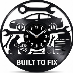 May include: Black vinyl record clock with a car silhouette, wrenches, and a mechanic. The clock face is black with white numbers and hands. The text "BUILT TO FIX" is at the bottom. A unique automotive-themed wall clock.