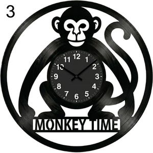Puede incluir: Reloj de pared negro con diseño de mono. La esfera del reloj es negra con números y manecillas blancas. Las palabras "MONKEY TIME" están recortadas en la parte inferior del reloj.