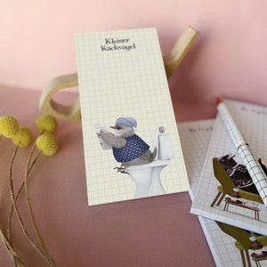 Könnte beinhalten: Ein gelber Notizblock mit Gittermuster und dem Text "Kleiner Kackvogel" oben. Ein Cartoon-Vogel mit blauem Hut und blauer Weste sitzt auf einer weißen Toilette und liest Zeitung.