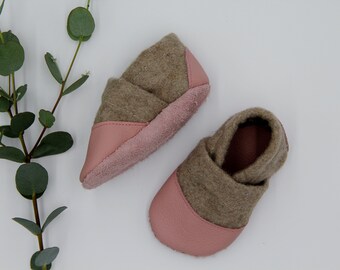 May include: A pair of soft, brown and pink baby booties. The booties are made of a soft, fuzzy material and have a leather sole.
