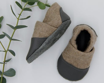 May include: A pair of gray and brown baby shoes with a soft, suede-like texture. The shoes have a leather sole and a fold-over cuff.