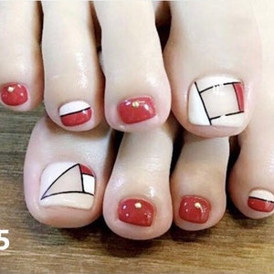 May include: Close-up of a foot with red and white geometric nail art designs. The nail art features a combination of red, white, and black colors, creating a modern and stylish look.