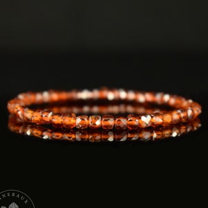 Peut inclure: Un bracelet composé de petites pierres précieuses facettées de couleur brun orangé. Le bracelet est sur un fond noir et reflète la lumière.