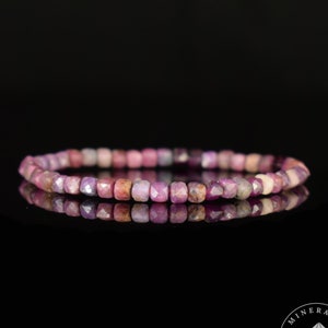 May include: A delicate bracelet composed of small, faceted, pink and purple gemstones. The beads are arranged in a single strand, reflecting light and creating a subtle sparkle. The bracelet is displayed against a black background.