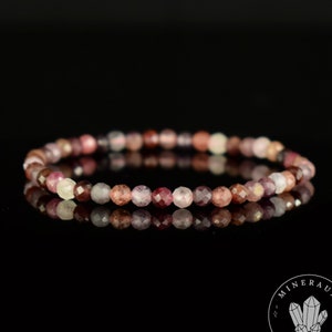 Op de afbeelding: Een armband gemaakt van kleine, gefacetteerde, roze, rode en paarse edelstenen. De armband ligt op een zwarte achtergrond.