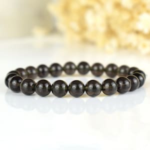 Peut inclure: Un bracelet noir composé de perles rondes et lisses. Le bracelet est posé à plat sur une surface blanche.