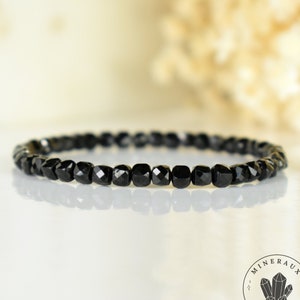 Può includere: Un braccialetto nero fatto con perline di onice nero sfaccettate. Il braccialetto è su una superficie bianca.