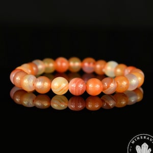 May include: A carnelian bracelet featuring orange and white banded beads. The bracelet is crafted from natural stones and measures approximately 7 inches in length.