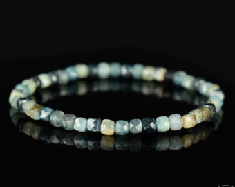 May include: A blue gemstone bracelet with faceted beads. The bracelet is made of small, square-shaped beads that are a mix of light and dark blue.