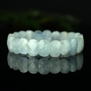 May include: A light blue aquamarine bracelet. The bracelet is made of faceted, oval-shaped stones. The stones are strung together to form a continuous loop. The bracelet is displayed on a reflective surface.