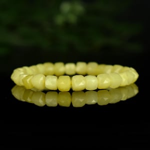 Peut inclure: Un bracelet de pierres précieuses jaunes avec des perles à facettes. Le bracelet est composé de pierres jaune clair translucides et se reflète sur une surface noire. Les perles sont de forme carrée et espacées uniformément.