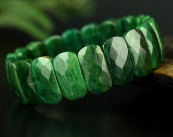 Può includere: Un braccialetto composto da molteplici perline di pietra preziosa verde scuro sfaccettate. Ogni perlina presenta una superficie lucida a più lati che riflette la luce, creando un aspetto strutturato lungo la fascia circolare del gioiello.