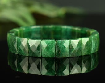 Può includere: Un braccialetto elastico composto da perline rettangolari in pietra preziosa verde sfaccettata. Le perline presentano una profonda tonalità smeraldo con variazioni naturali di colore e consistenza, disposte in un cerchio continuo.