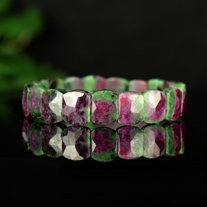 Op de afbeelding: Een armband gemaakt van groene en roze edelsteen kralen. De kralen zijn gefacetteerd en hebben een vierkante vorm.
