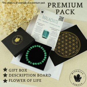 May include: A premium pack featuring a green malachite bracelet in a black gift box. The set includes a description board and a black card with a gold flower of life design. The text on the description board is in French.