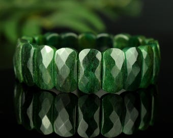 Può includere: Un braccialetto composto da numerose perline rettangolari sfaccettate di colore verde scuro disposte in un cerchio continuo. Ogni perlina presenta molteplici superfici piatte e angolate che catturano la luce, creando un aspetto riflettente.