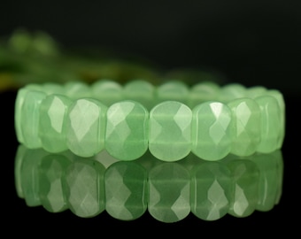 Può includere: Un braccialetto elastico composto da perline ovali sfaccettate di colore verde chiaro. Le perline hanno una finitura liscia e lucida con molteplici superfici piatte che catturano la luce, creando un motivo ripetitivo lungo tutta la circonferenza.