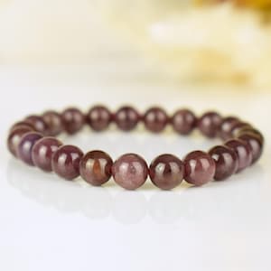 May include: A stretch bracelet composed of smooth, round, deep reddish-purple beads. The beads exhibit a polished, reflective surface with subtle variations in color intensity, arranged in a continuous circular loop on a flexible cord.