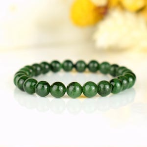 May include: A dark green beaded bracelet. The bracelet is made of round, polished beads. The beads have a glossy finish and reflect light. The bracelet is displayed on a white surface.
