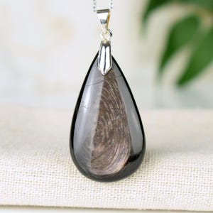 May include: A teardrop-shaped pendant made of black obsidian with a silver bail. The obsidian has a unique pattern of swirling lines.