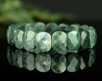 Può includere: Un braccialetto elastico composto da perline di agata muschiata di forma ovale e sfaccettata. Le perline presentano un motivo variegato di verde bosco profondo, verde chiaro traslucido e inclusioni bianche, creando un aspetto naturale e marmorizzato.
