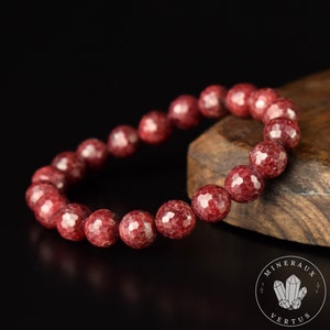 Peut inclure: Un bracelet en pierres précieuses rouges composé de perles facettées. Le bracelet est posé sur une surface en bois.