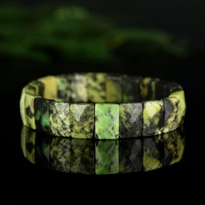 Peut inclure: Un bracelet en pierres précieuses vertes et noires avec des perles de forme carrée. Le bracelet est fait de pierres naturelles et a une finition polie.