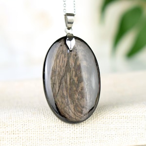 Puede incluir: Un collar de cadena de plata con un colgante redondo de piedra negra y gris. La piedra tiene un patrón único y arremolinado.