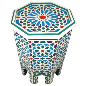 Può includere: Un tavolino ottagonale con un motivo geometrico nei toni del blu, verde, rosso e viola. Il tavolo ha un bordo e gambe bianche e il piano presenta un disegno a stella. Il tavolo è alto circa 50 cm.