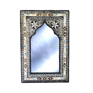 May include: A decorative mirror with an ornate, arched frame. The frame is made of wood and metal and is decorated with intricate carvings and inlays. The mirror is surrounded by a border of small, round beads.