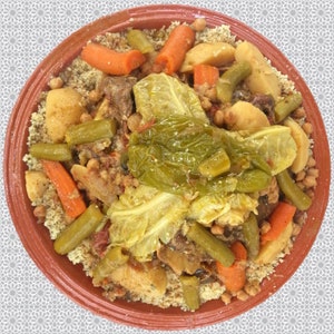 May include: A close-up of a traditional Moroccan dish called couscous, served in a terracotta bowl. The couscous is topped with a variety of vegetables, including carrots, green beans, potatoes, and cabbage. There is also a generous amount of meat in the dish.