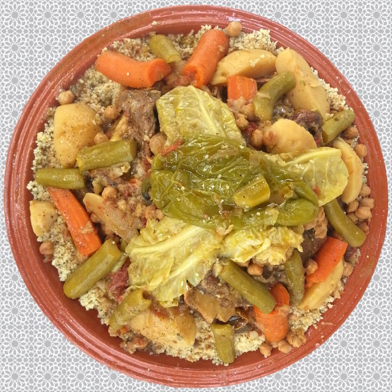 May include: A close-up of a traditional Moroccan dish called couscous, served in a terracotta bowl. The couscous is topped with a variety of vegetables, including carrots, green beans, potatoes, and cabbage. There is also a generous amount of meat in the dish.