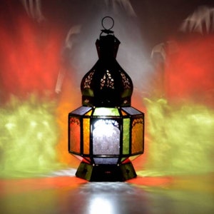 Può includere: Una lanterna marocchina decorativa con un design in vetro colorato. La lanterna è in metallo e ha una parte superiore rotonda a forma di cupola. La lanterna è illuminata dall'interno, proiettando un bagliore caldo.