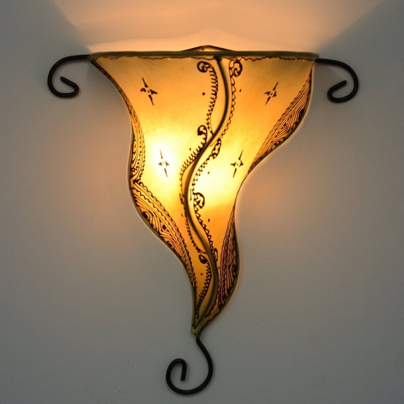 May include: A wall-mounted light fixture with a decorative, hand-painted, yellow paper shade. The shade features a swirling, intricate design with black accents. The fixture has a black metal frame with a curved arm.