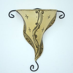 May include: A cream-colored wall sconce with a black metal frame and intricate black designs. The sconce is shaped like a teardrop and has a curved top.